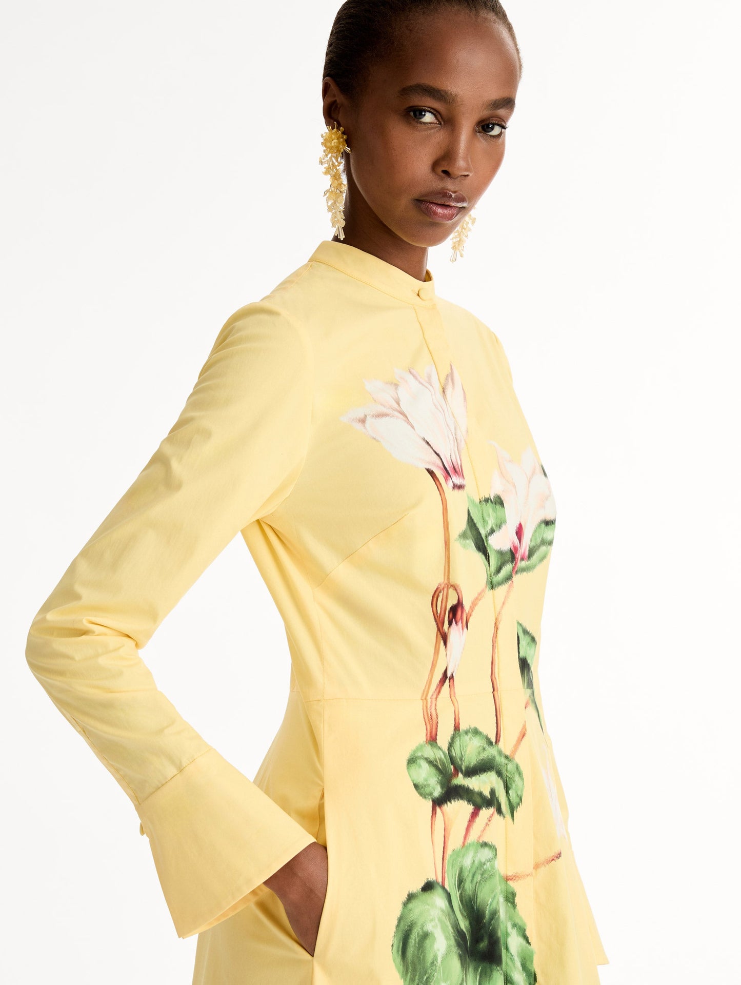 Yellow cotton poplin caftan with a mandarin collar and concealed button front. Chiné Cyclamen motif softly blurred, edges. Full-length sleeves. Close Up Side View.