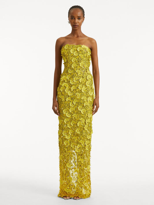 Full body front view of model wearing a yellow gown with peony raffia and sequin embroidery. With a strapless neckline and column silhouette.