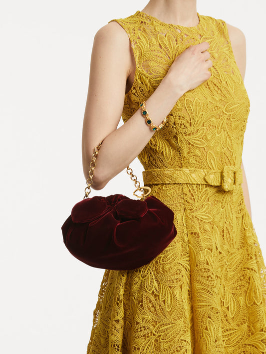 On model photo of The Velvet Clutch which features dark red fabric folding, where the velvet is gathered and secured with a voluminous bow and a gold chain with the Oscar 'O'.