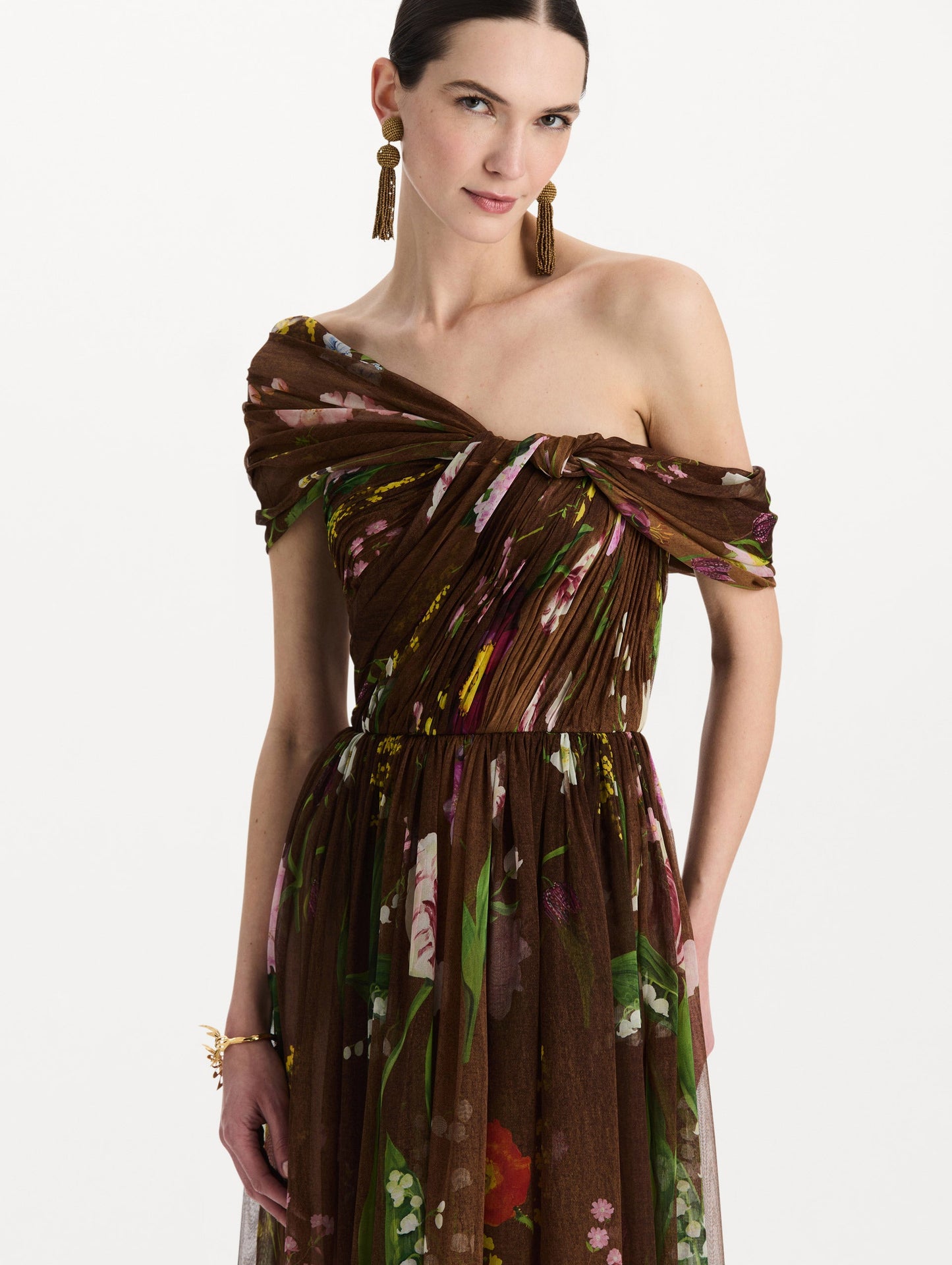 The model is wearing the mixed botanical silk chiffon gown with a one-shoulder neckline and a painterly floral print in a brown multi palette. Zoom view.