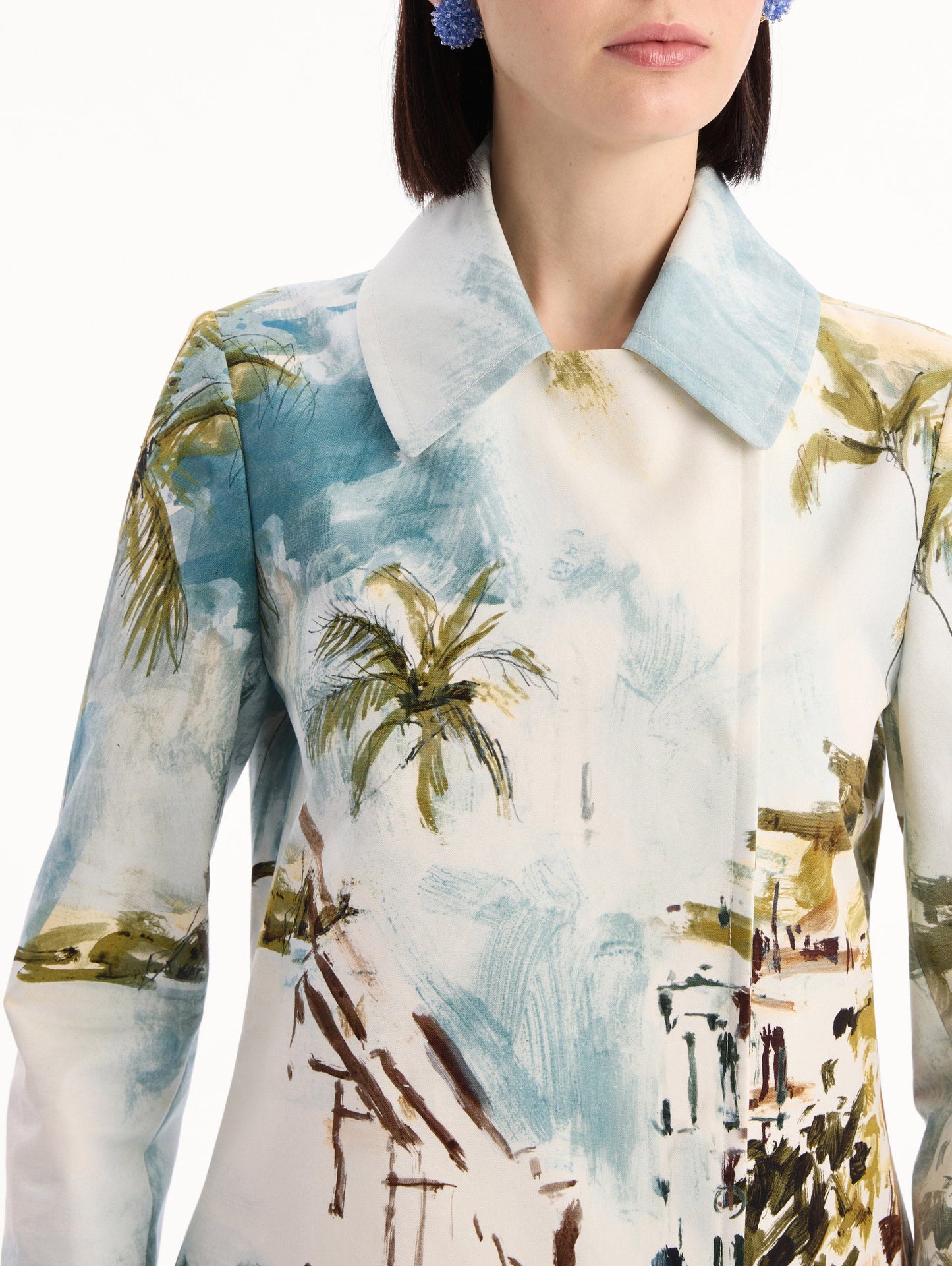 The model is wearing the Dominican Landscape Cotton Poplin Coat featuring an exaggerated collar, hidden buttons, front-flap pockets, and long sleeves. Detail View.