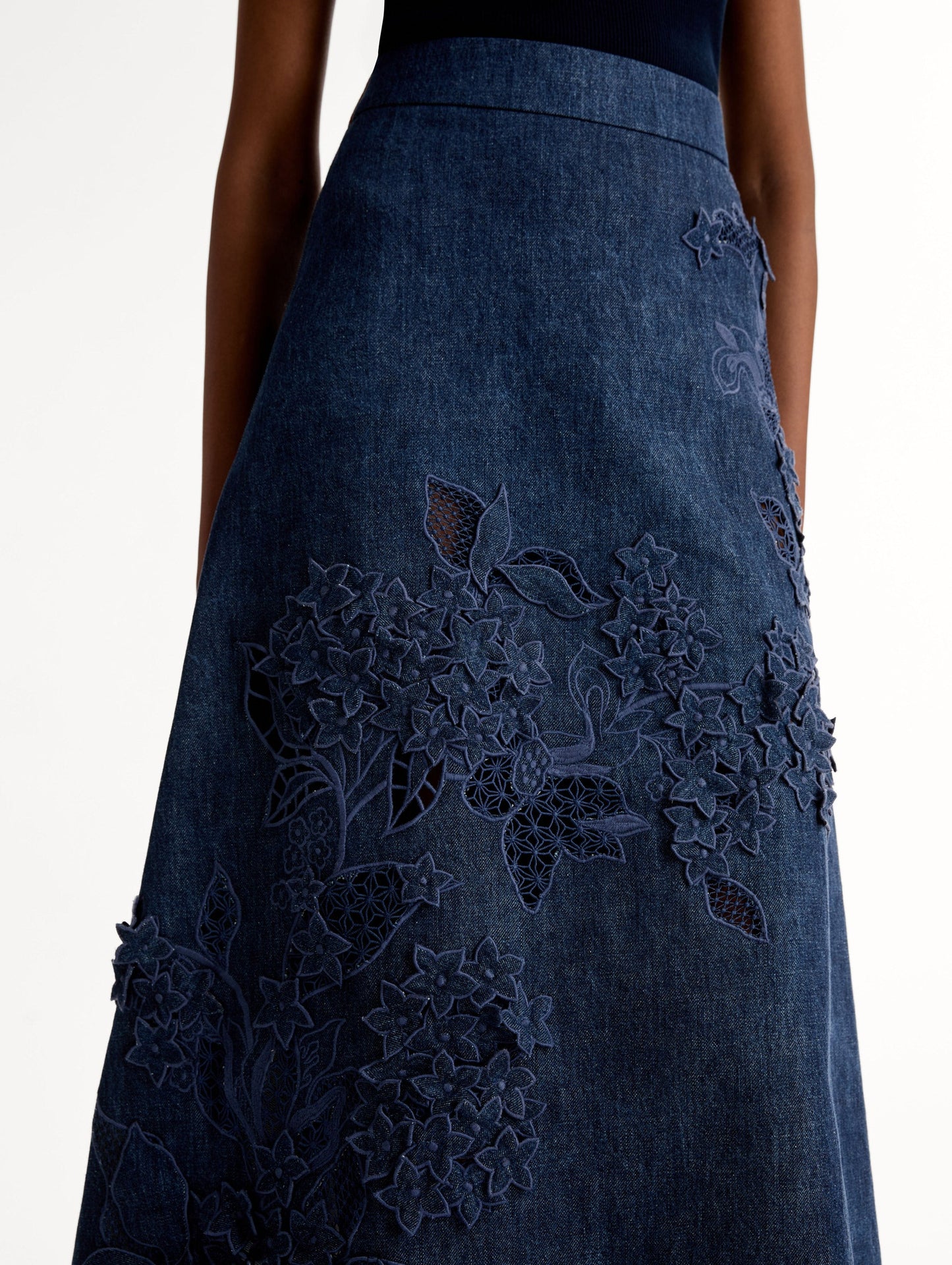 High waisted denim skirt with intricate porcelain flower threadwork. Classic A-line silhouette. Mid length. Side View, Close Up.