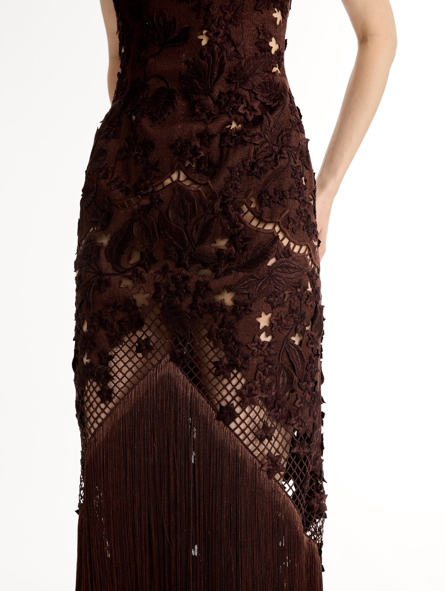 Mahogany strapless floor length gown with Porcelain flower threadwork in sculptural cutouts with glimpses of skin. Intricate lattice motifs. The silhouette elongates before cascading into a curtain of fringe. Front View, Close Up.
