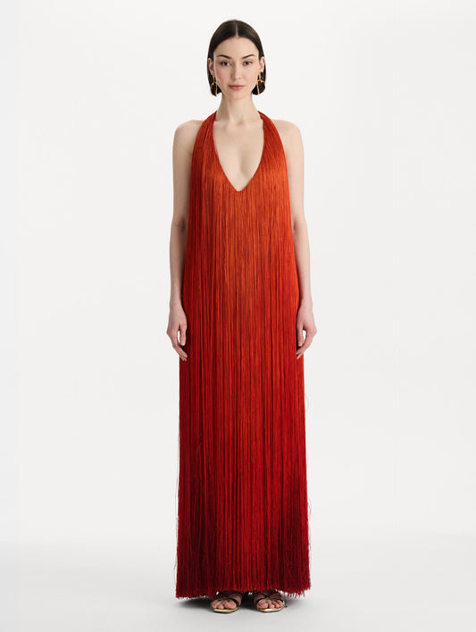 The model is wearing the Ombré Fringe Gown in Paprika Red. Featuring a deep, halter neckline, and full fringe silhouette. Front View.