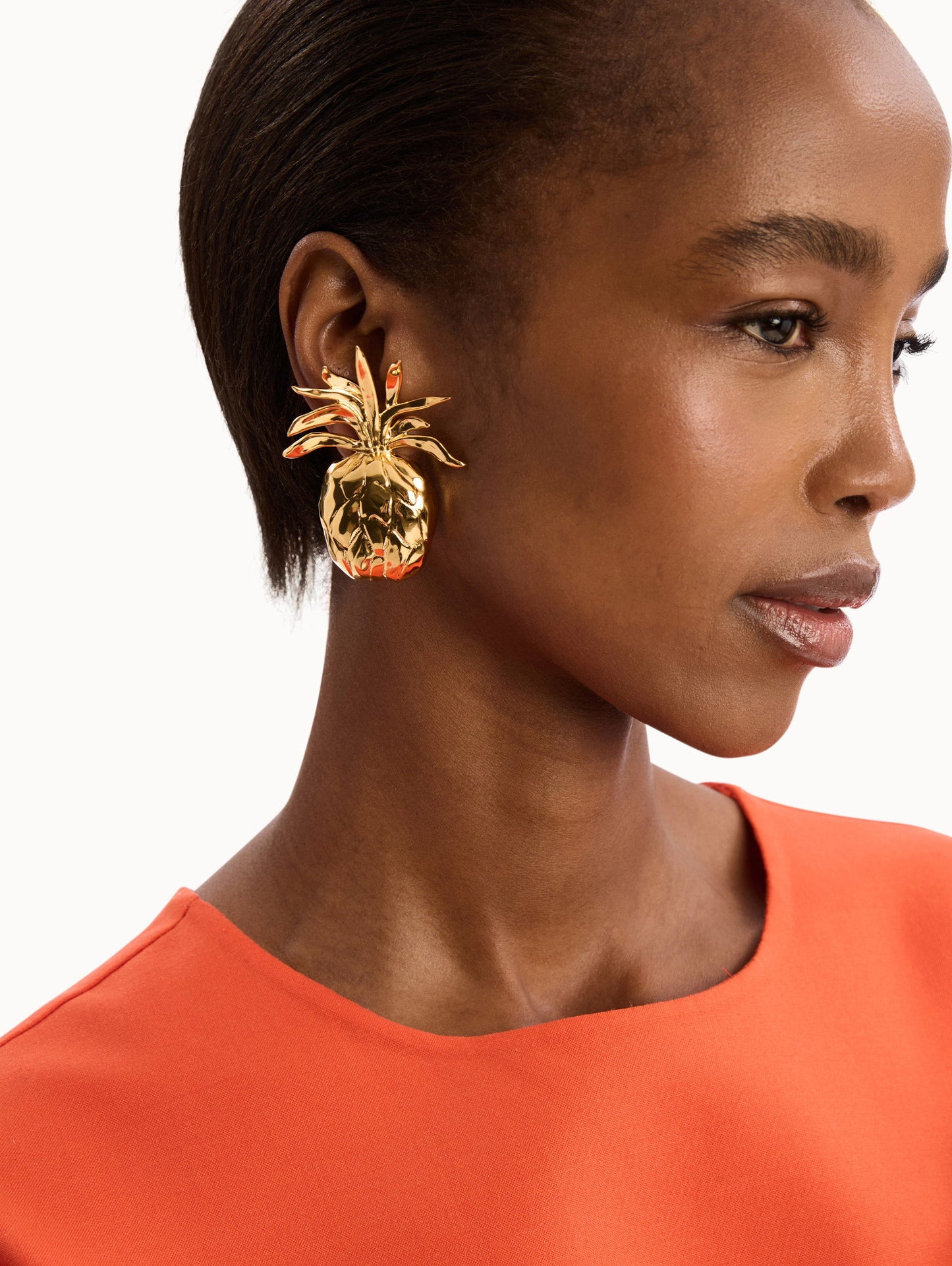 The model is wearing the Large Gold Pineapple Cutout Clip-On Earrings. Detail View.