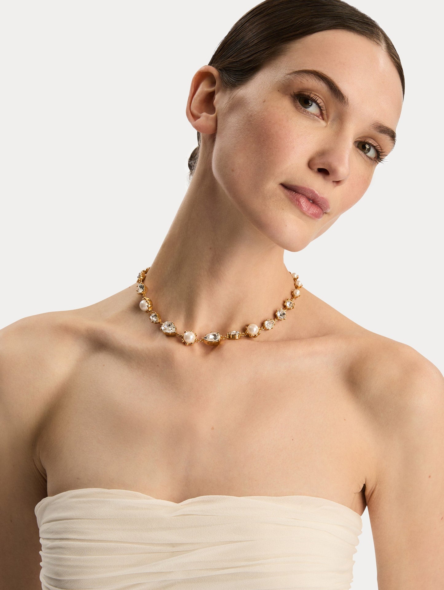 Gold Faceted Crystal Necklace featuring alternating white pearls and clear crystal settings in a graduated design. Front View.