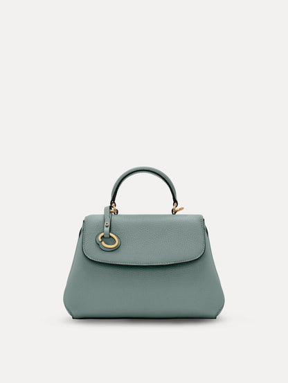 The Mini Poppy handbag in a Mint color with an Oscar O logo tag around the top handle, paired with a floral white dress. Front View.