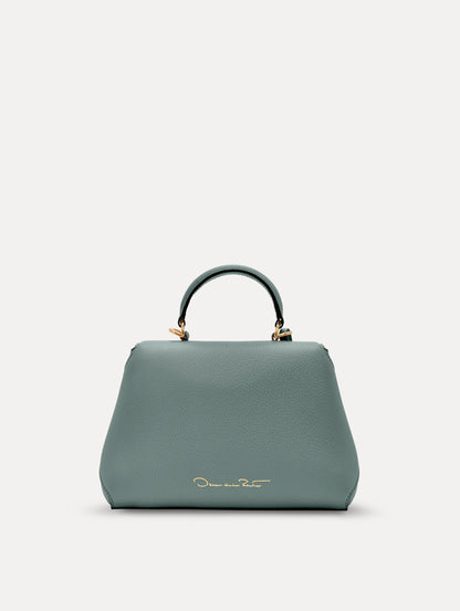 The Mini Poppy handbag in a Mint color with an Oscar O logo tag around the top handle, paired with a floral white dress. Back View.