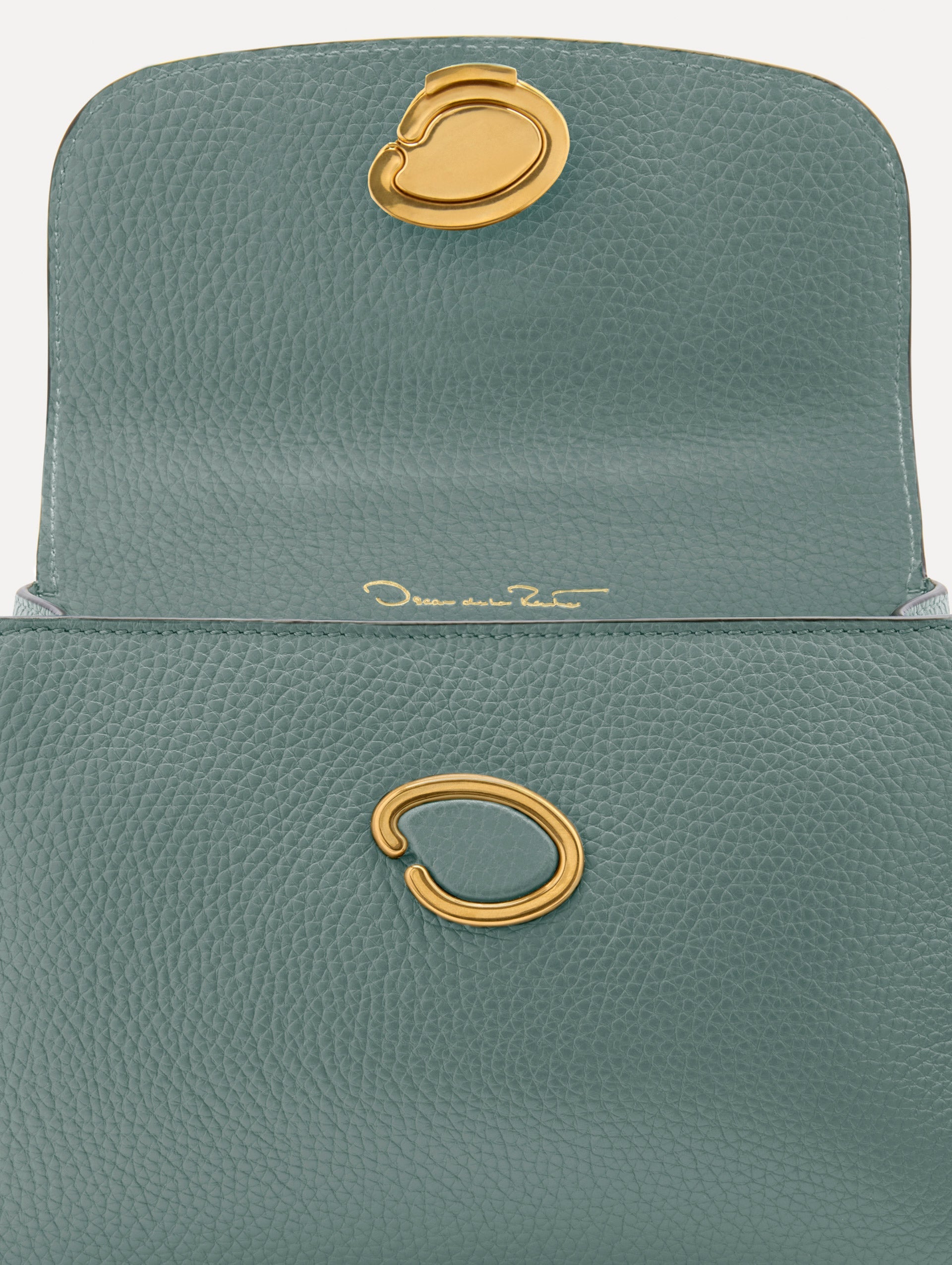 The Mini Poppy handbag in a Mint color with an Oscar O logo tag around the top handle, paired with a floral white dress. Zoom View.