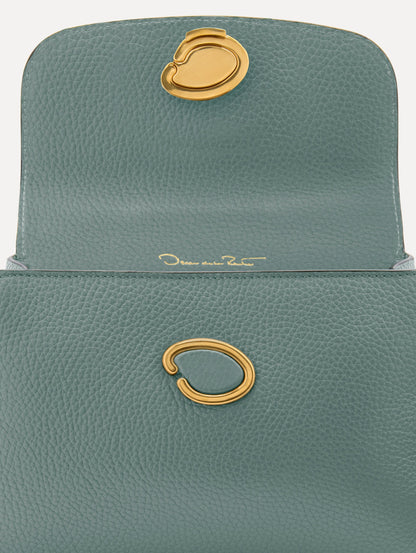 The Mini Poppy handbag in a Mint color with an Oscar O logo tag around the top handle, paired with a floral white dress. Zoom View.