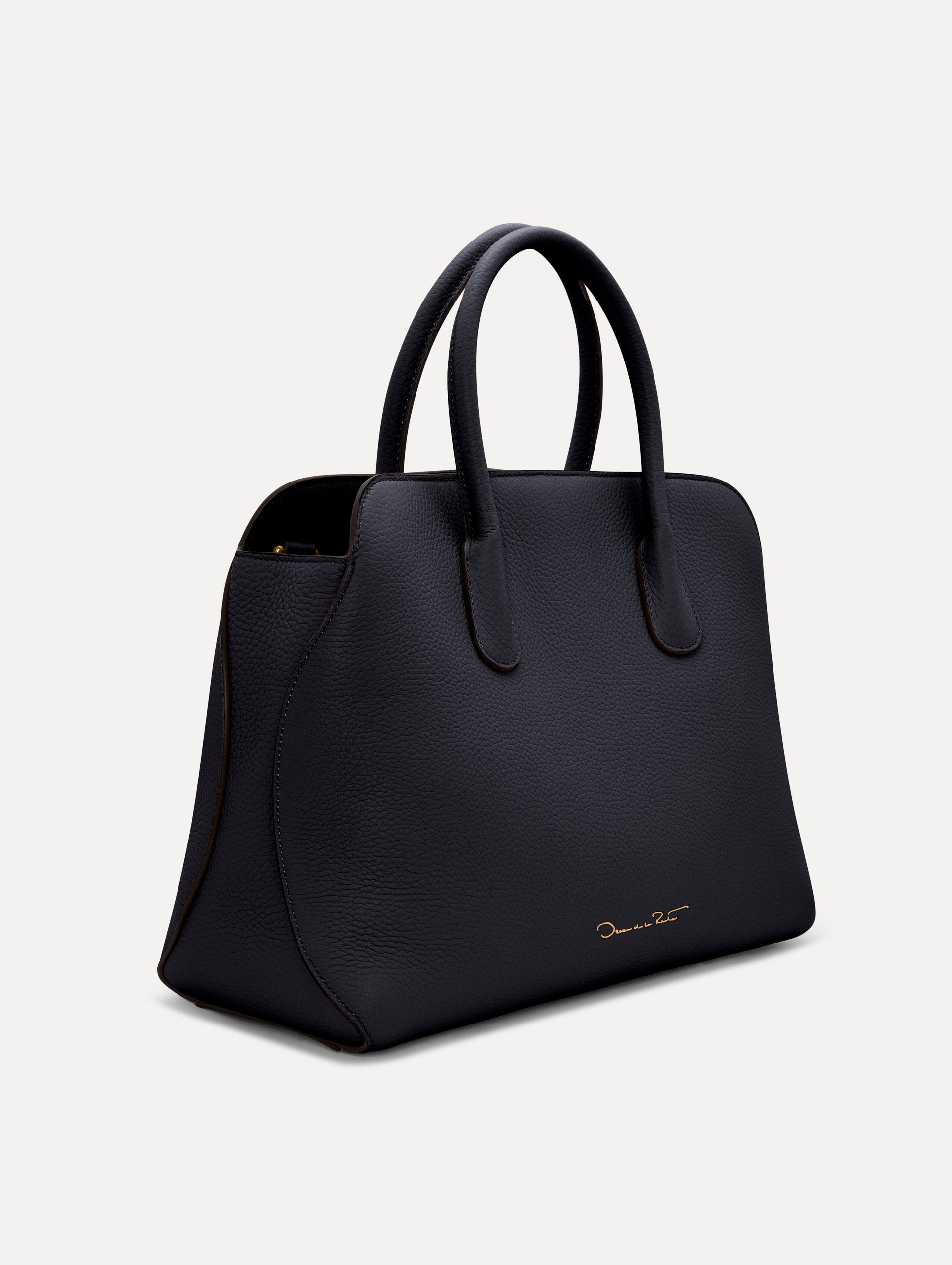 The Ivy top handle handbag in black, paired with some khaki pants. The bag comes with the Oscar O logo as a tag around the handle. Side View.