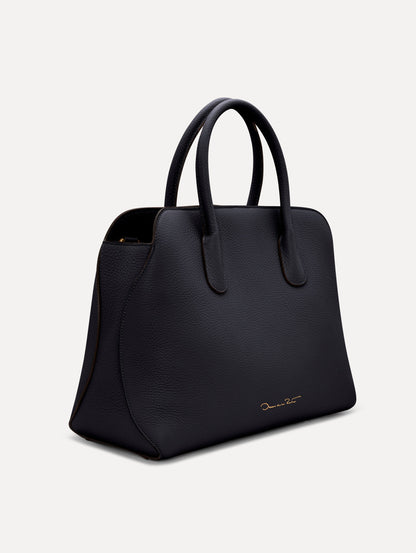 The Ivy top handle handbag in black, paired with some khaki pants. The bag comes with the Oscar O logo as a tag around the handle. Side View.