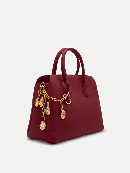 Pink, Orange, and Blue Crystals O Bag Charm in Gold styled with a red top handle handbag. Front View