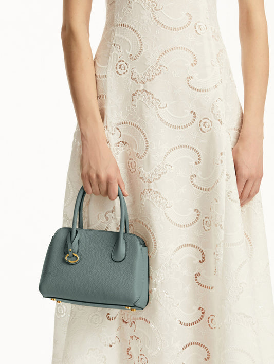 Mini Ivy in a light mint color. The Mini Ivy is a top handle bag with a detachable shoulder strap, and it has the Oscar O logo attached around the top handle. Front View.