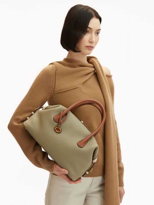 Model in Brown Sweater and White pants Wearing The Dahlia Duffle Bag in Sage Green with Brown Top Handle. Front View