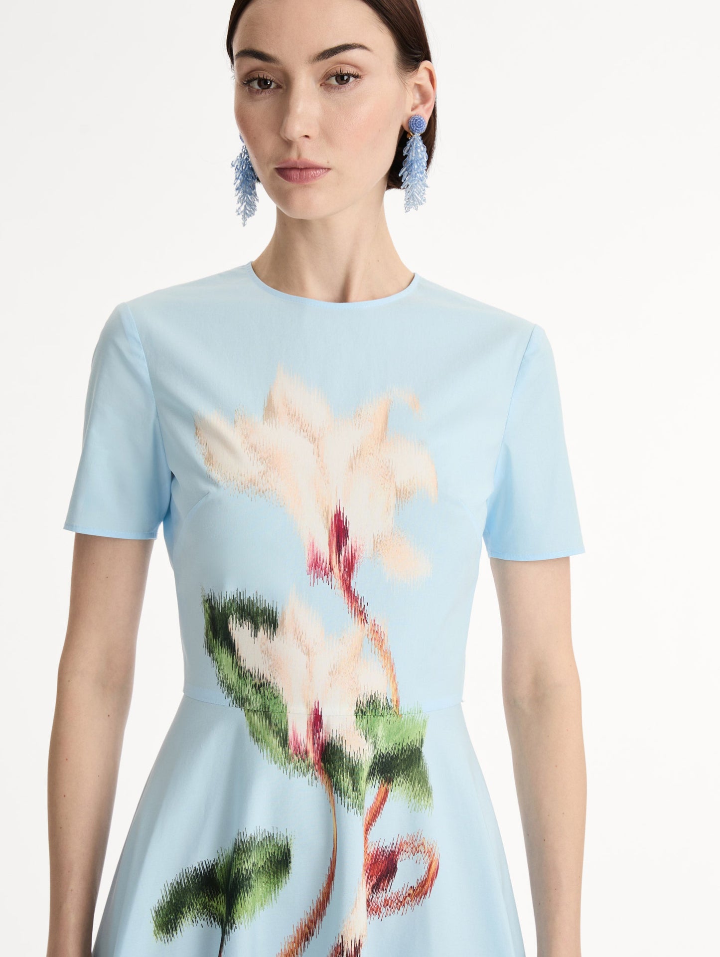 Short sleeve, light blue cotton poplin midi dress. Fitted bodice, full A-line skirt. Chiné Cyclamen motif with blurred, edges. Front View, Close Up.
