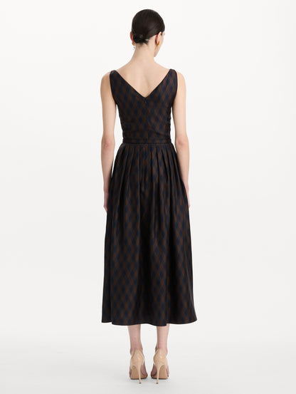 The model is wearing the argyle silk twill dress with a sleeveless silhouette, a V-neckline, and an argyle print in navy and brown. Back view.