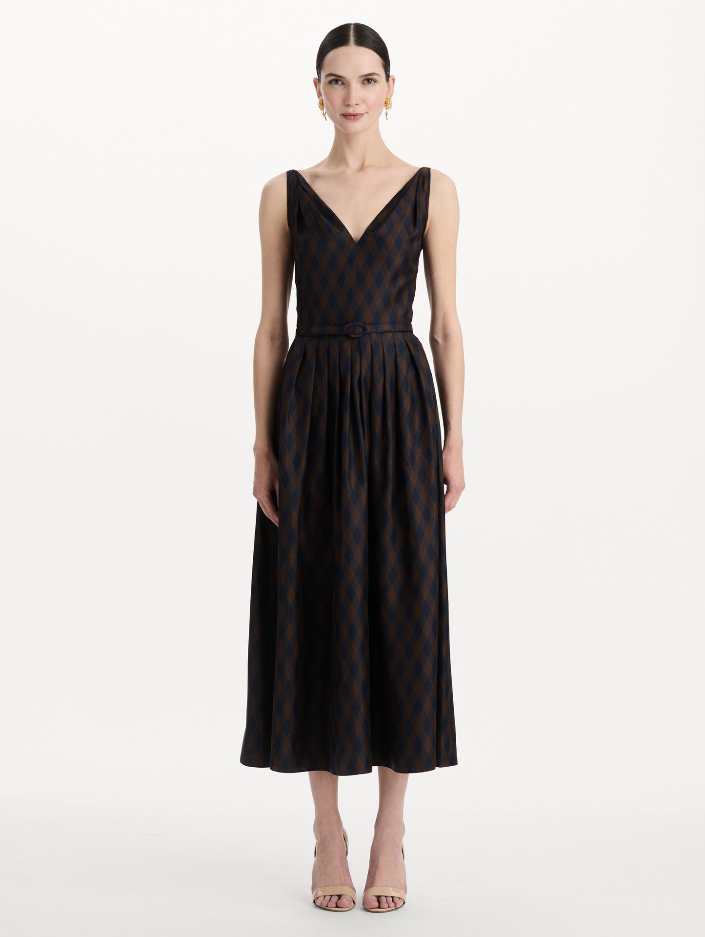 The model is wearing the argyle silk twill dress with a sleeveless silhouette, a V-neckline, and an argyle print in navy and brown. Front view.