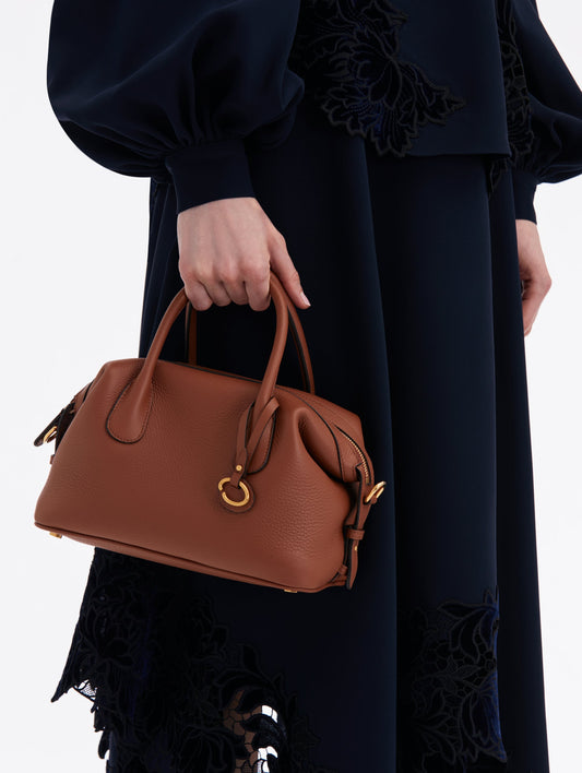Cognac Brown Handbag, with Top Handle, Crossbody Strap, and Oscar logo around the Handle. Front View.