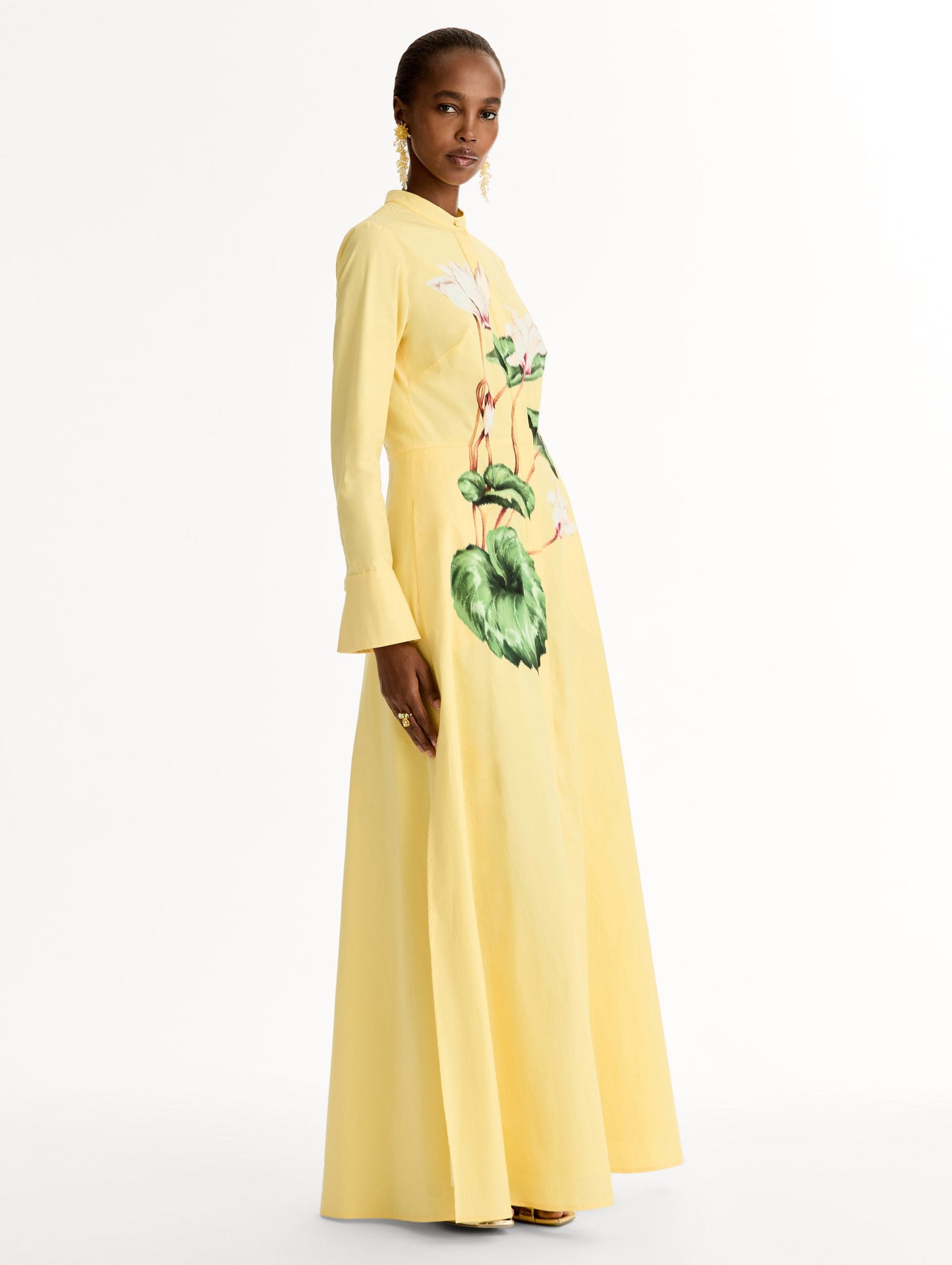 Yellow cotton poplin caftan with a mandarin collar and concealed button front. Chiné Cyclamen motif softly blurred, edges. Full-length sleeves. Side View.