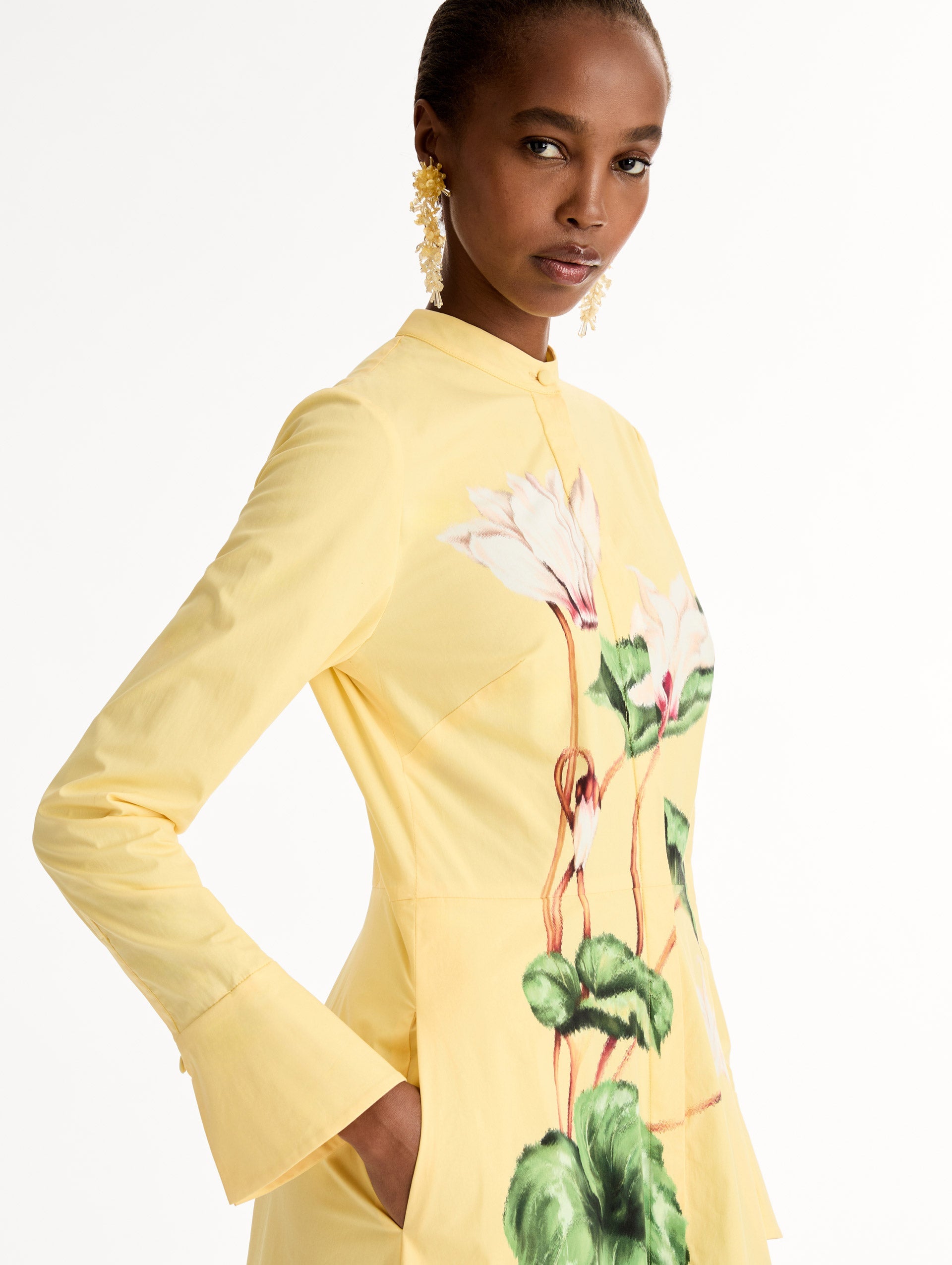 Yellow cotton poplin caftan with a mandarin collar and concealed button front. Chiné Cyclamen motif softly blurred, edges. Full-length sleeves. Close Up Side View.