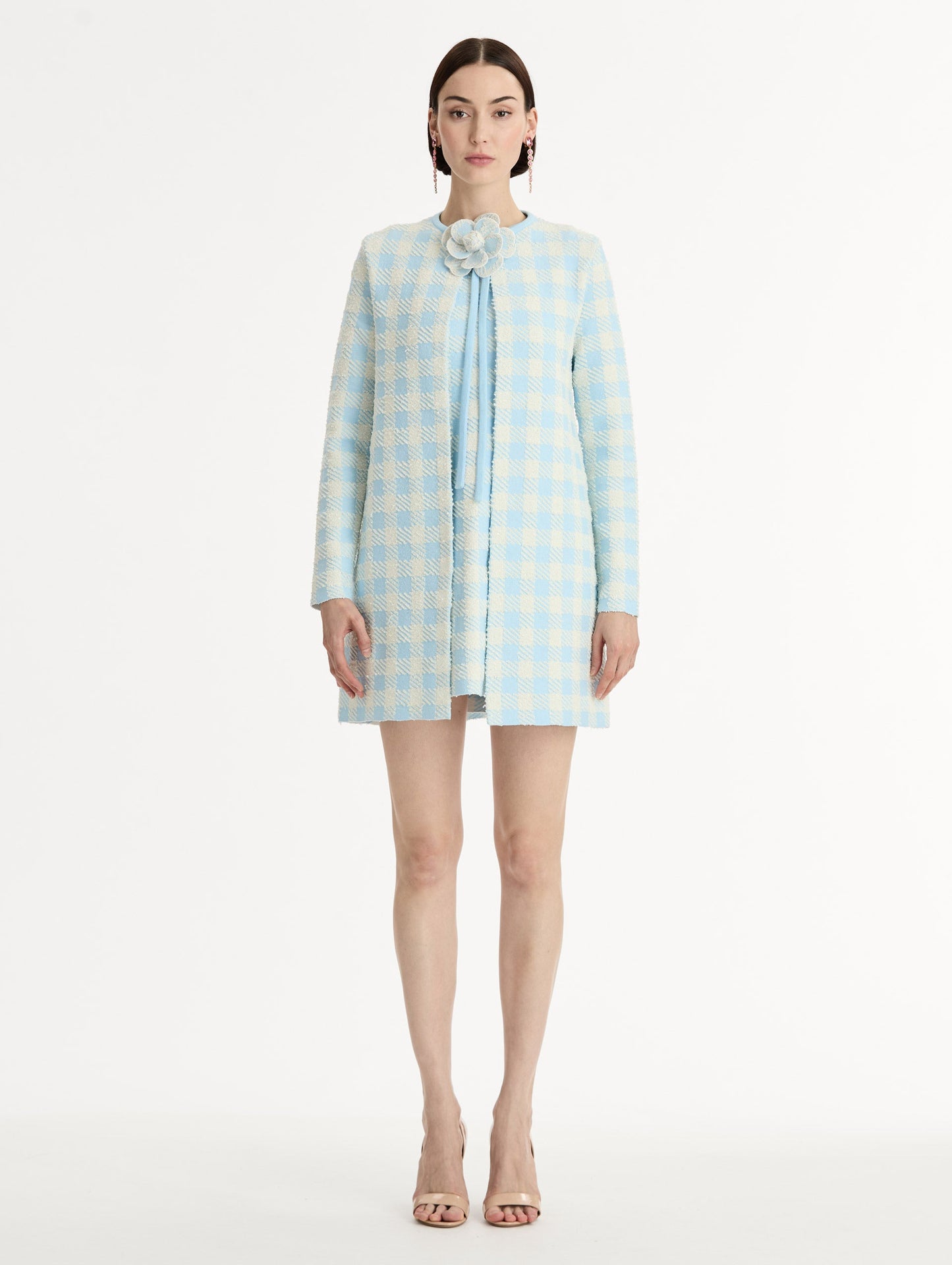 Textured jacquard, long sleeve coat in pale blue and ivory gingham pattern. Streamlined silhouette with a floral appliqué at the neckline. Front View.