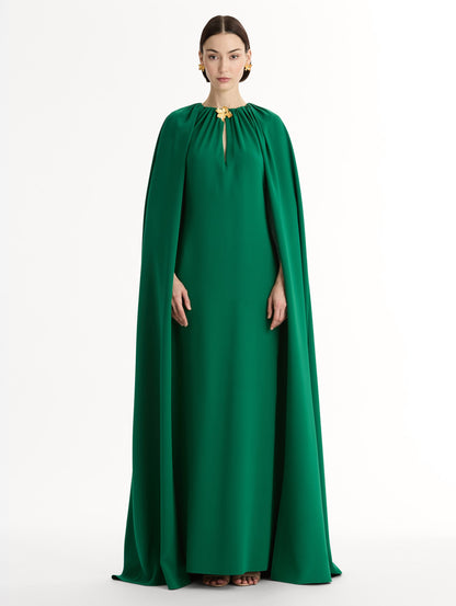 Emerald georgette caftan with fluid silhouette. Singular gilded cyclamen detail offers a sculptural focal point. Sweeping cape-like shape. Front View.