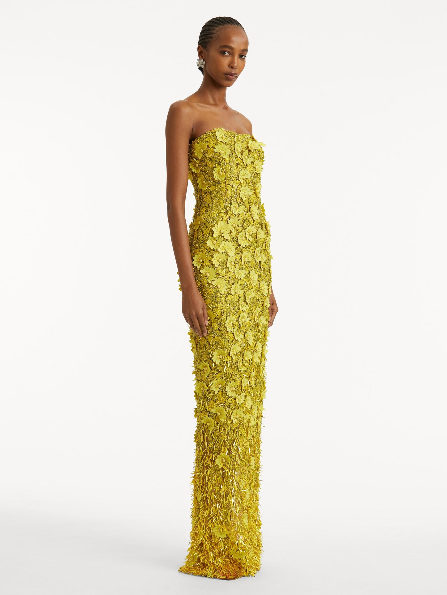 Full body side view of model wearing a yellow gown with peony raffia and sequin embroidery. With a strapless neckline and column silhouette.
