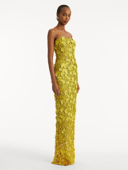 Full body side view of model wearing a yellow gown with peony raffia and sequin embroidery. With a strapless neckline and column silhouette.