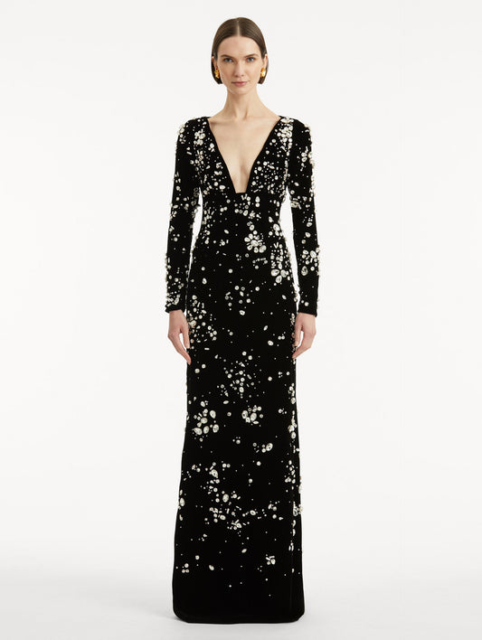 Full body front view of model wearing a long sleeve black gown with multi-dimensional stones scattered across the dress, features plunging V-neckline and column silhouette.