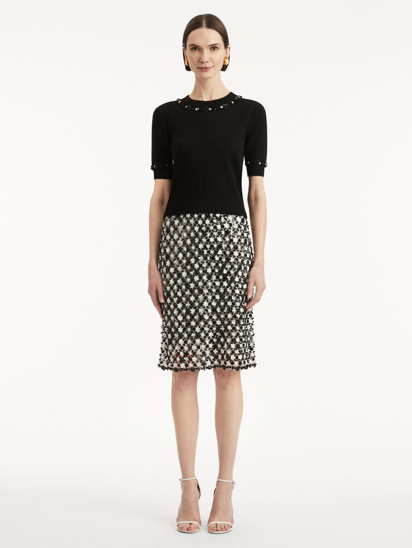 Full body front view of model wearing a short sleeve black pullover with a crew neckline and intricate sequin embroidery of ivory and noir florets which trace the trim