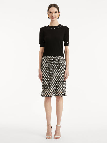 Full body front view of model wearing a short sleeve black pullover with a crew neckline and intricate sequin embroidery of ivory and noir florets which trace the trim