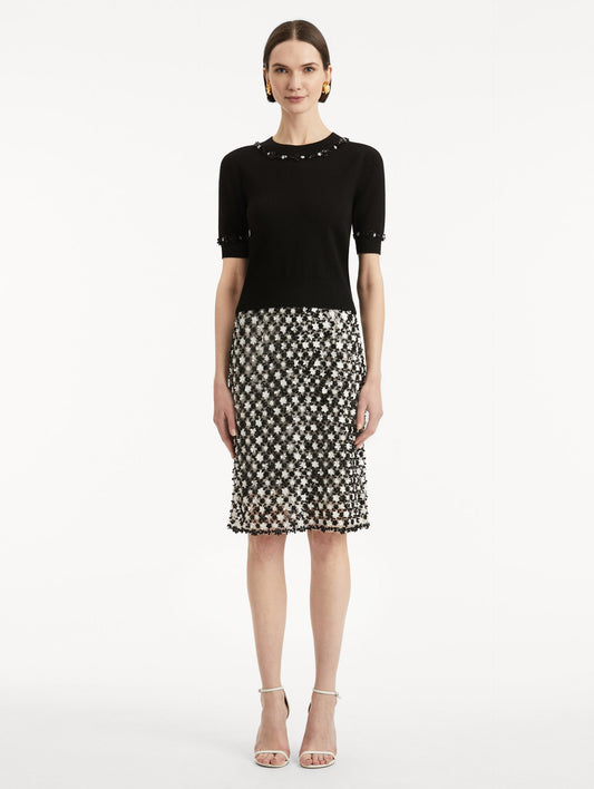 Full body front view of model wearing a short sleeve black pullover with a crew neckline and intricate sequin embroidery of ivory and noir florets which trace the trim