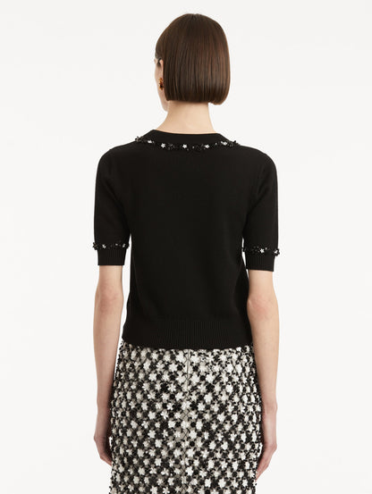 Back view of model wearing a short sleeve black pullover with a crew neckline and intricate sequin embroidery of ivory and noir florets which trace the trim