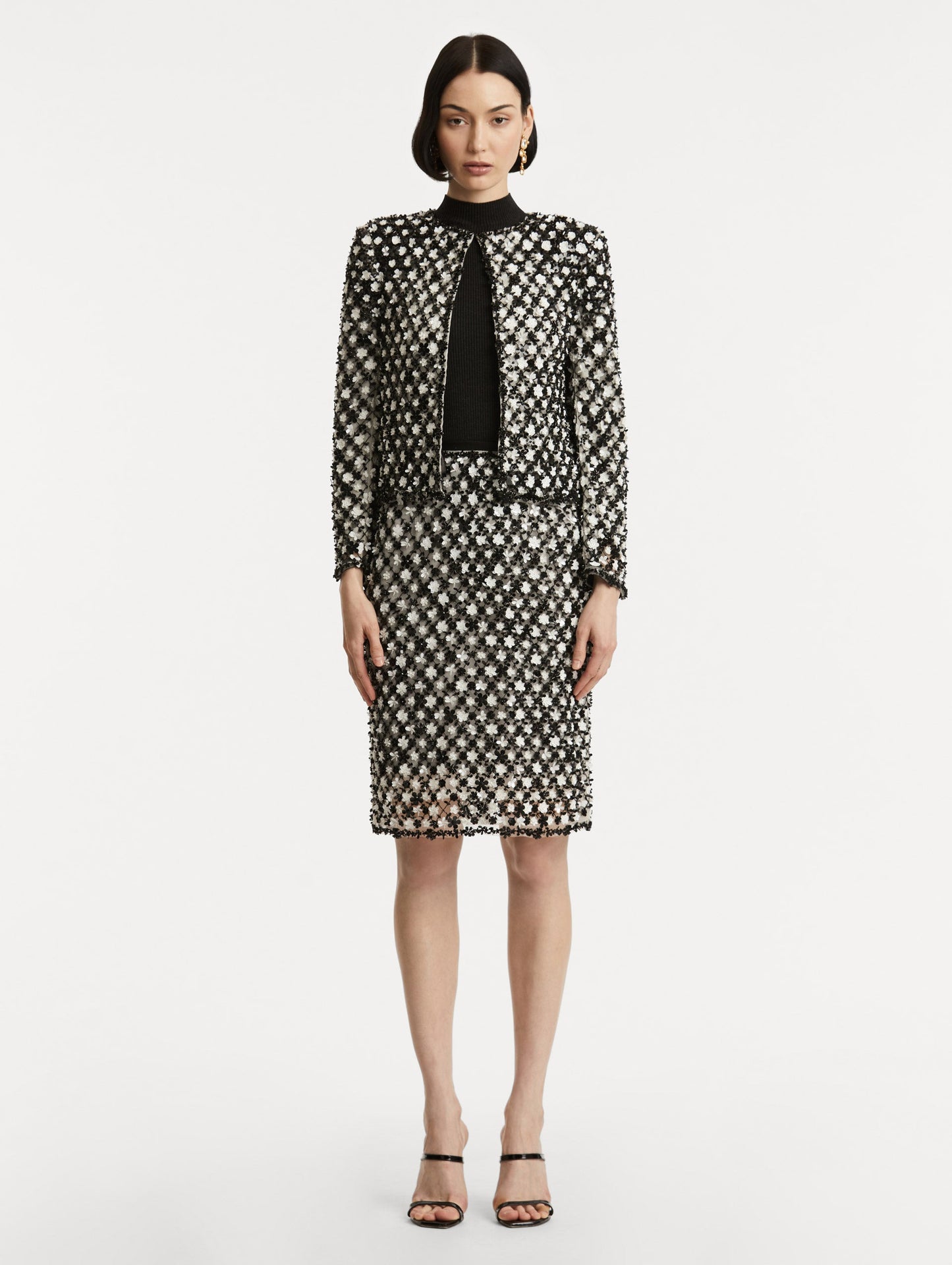 Full body front view of model wearing black and ivory long sleeve jacket with sequin embroidery, where florets create a tweed pattern.