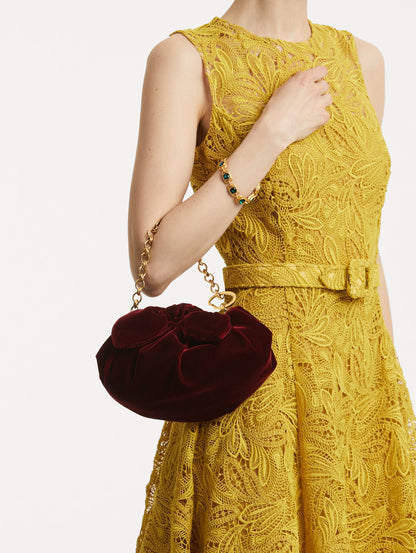 On model photo of The Velvet Clutch which features dark red fabric folding, where the velvet is gathered and secured with a voluminous bow and a gold chain with the Oscar 'O'.