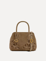 The Mini Ivy With Laser Cut Flowers in taupe has a compartment with top handles and a removeable shoulder strap with various Oscar 'O' emblems on the hangtag and magnetic closure.