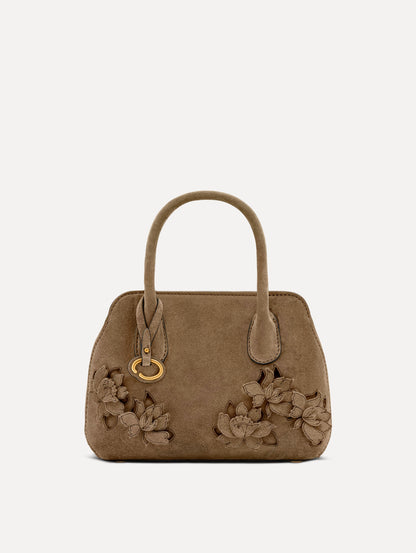 Front view of The Mini Ivy With Laser Cut Flowers in taupe which has a compartment with top handles and various Oscar 'O' emblems on the hangtag and magnetic closure.