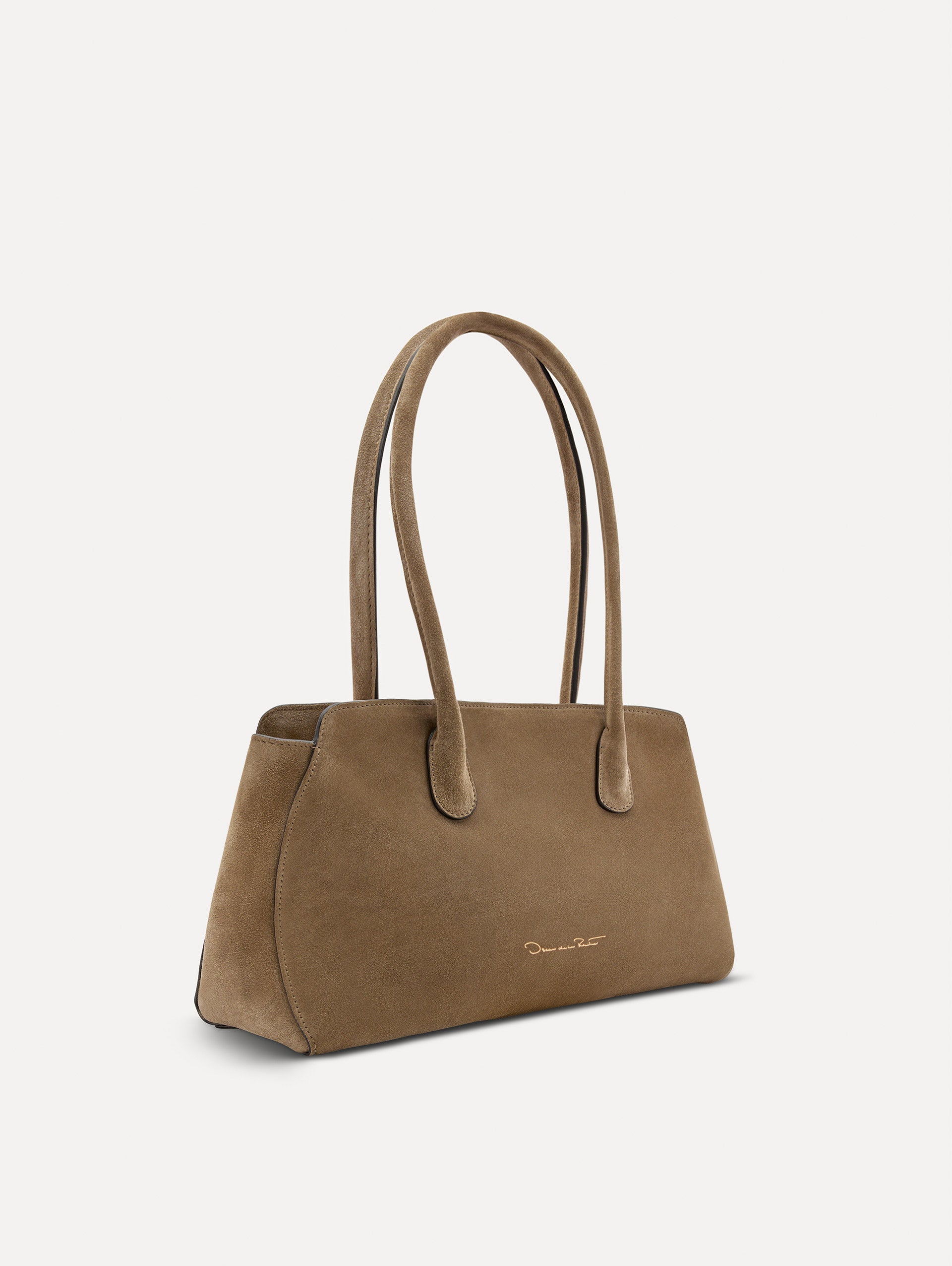 Side view of The Aster in taupe which features gently curved sides which mimic the Oscar 'O.' Elongated top handles with gold hardware and an emblem-stamped tag.