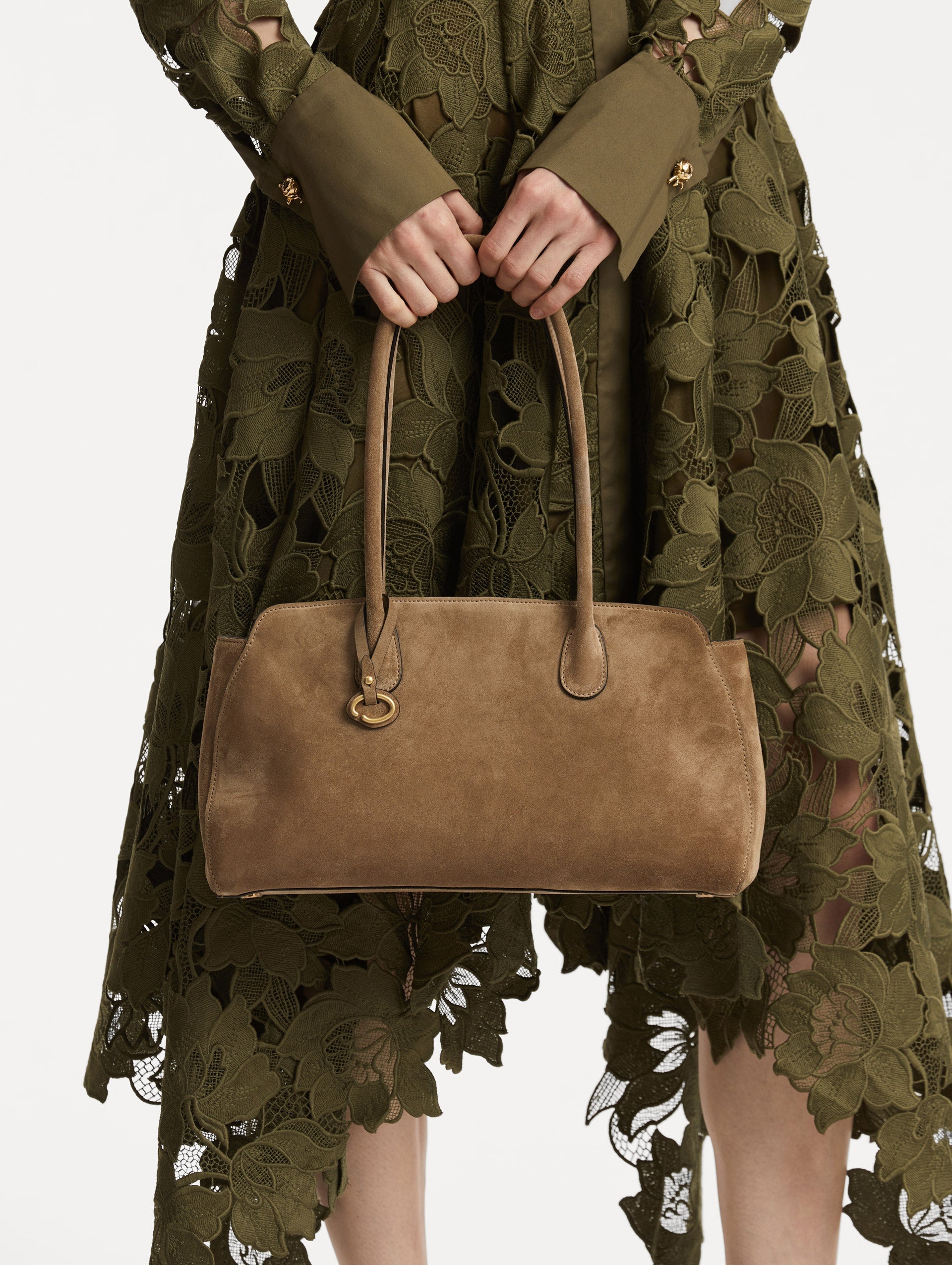 On model image of The Aster in taupe which features decisive lines and gently curved sides that mimic the Oscar 'O.' Elongated top handles and gold hardware and an emblem-stamped tag.