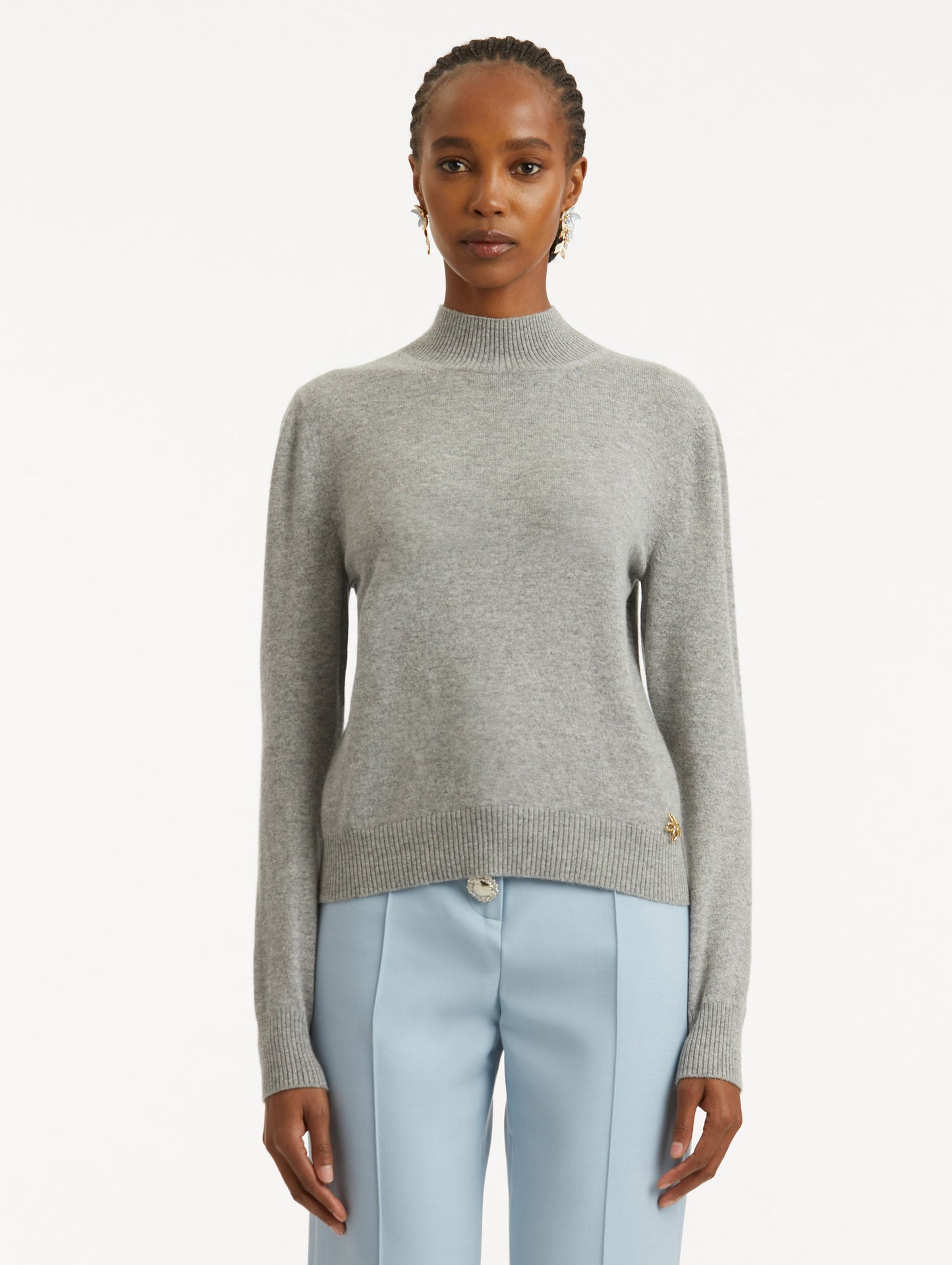 Front view of model wearing light grey pullover with long sleeves and a crew neckline. Features gold 'O' Flower emblem made of the interlocking Oscar 'O'.