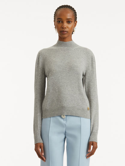 Front view of model wearing light grey pullover with long sleeves and a crew neckline. Features gold 'O' Flower emblem made of the interlocking Oscar 'O'.