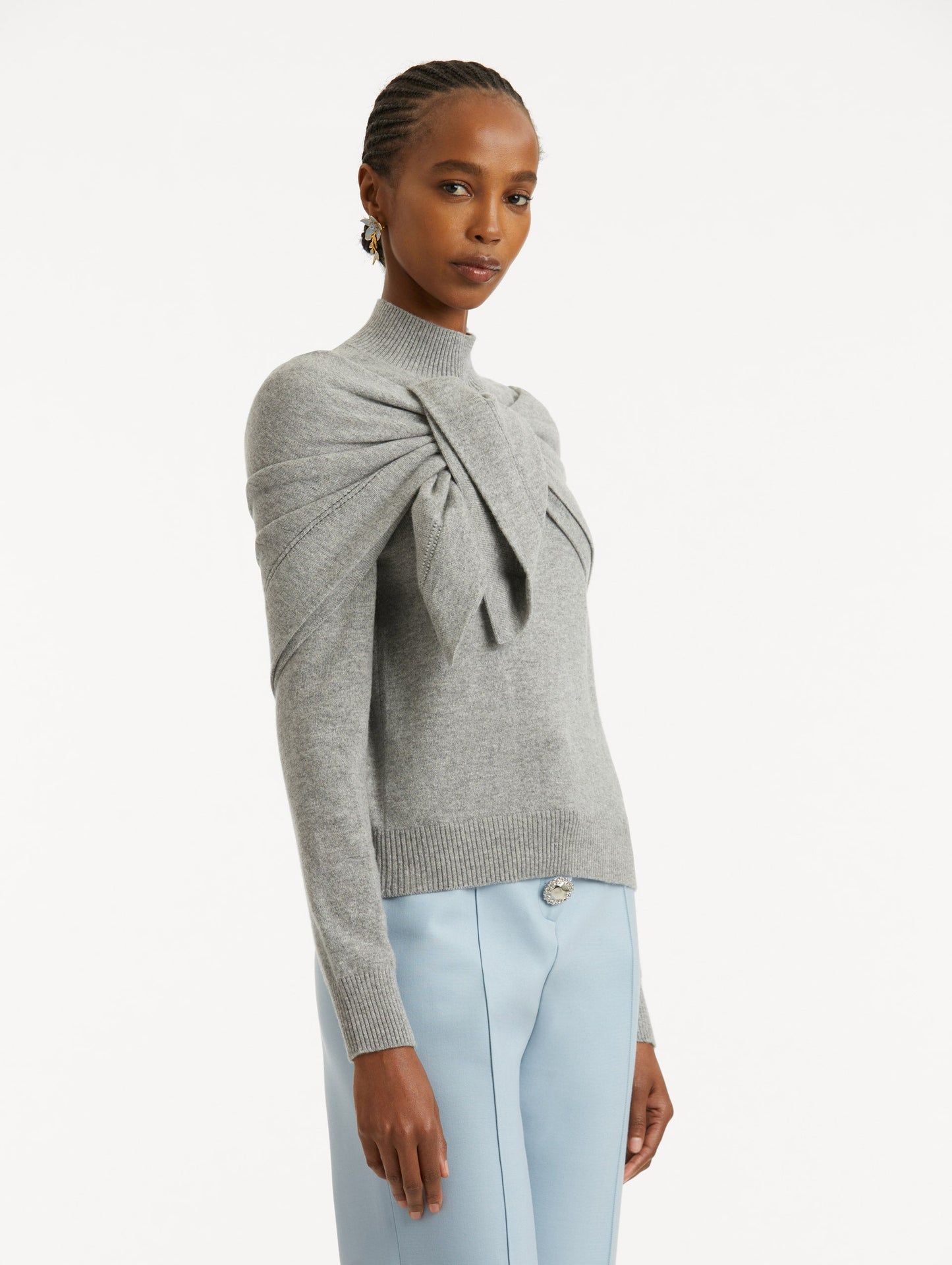 Side view of model wearing light grey pullover with long sleeves and a crew neckline. Features 'O' Flower emblem made of the interlocking Oscar 'O' and shawl draped over shoulders and tied in front.