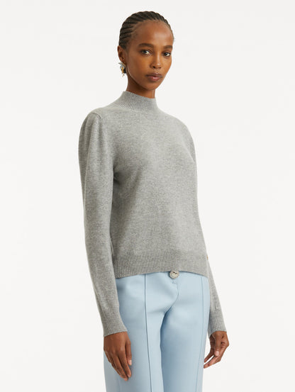 Side view of model wearing light grey pullover with long sleeves and a crew neckline.