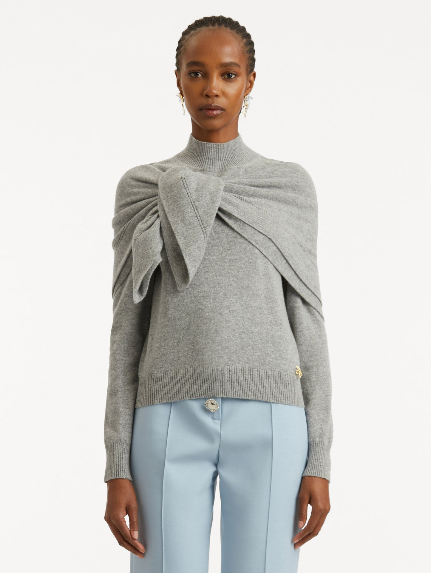 Front view of model wearing light grey pullover with long sleeves and a crew neckline. Features gold 'O' Flower emblem made of the interlocking Oscar 'O' and shawl draped over shoulders and tied in front.