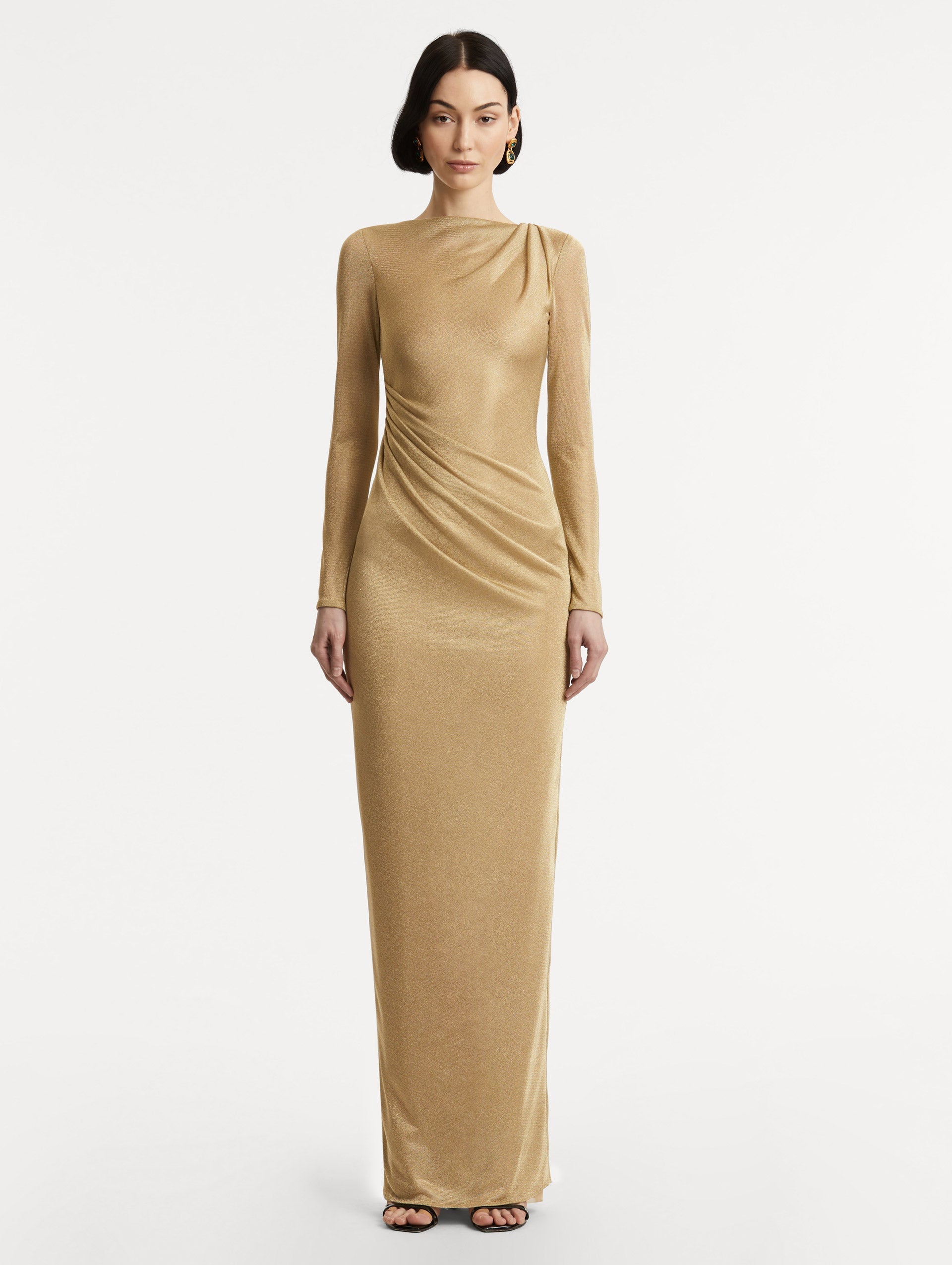 Full body front view image of model wearing a gold metallic jersey gown with a high neckline and long sleeves with draping at the shoulder and waist.