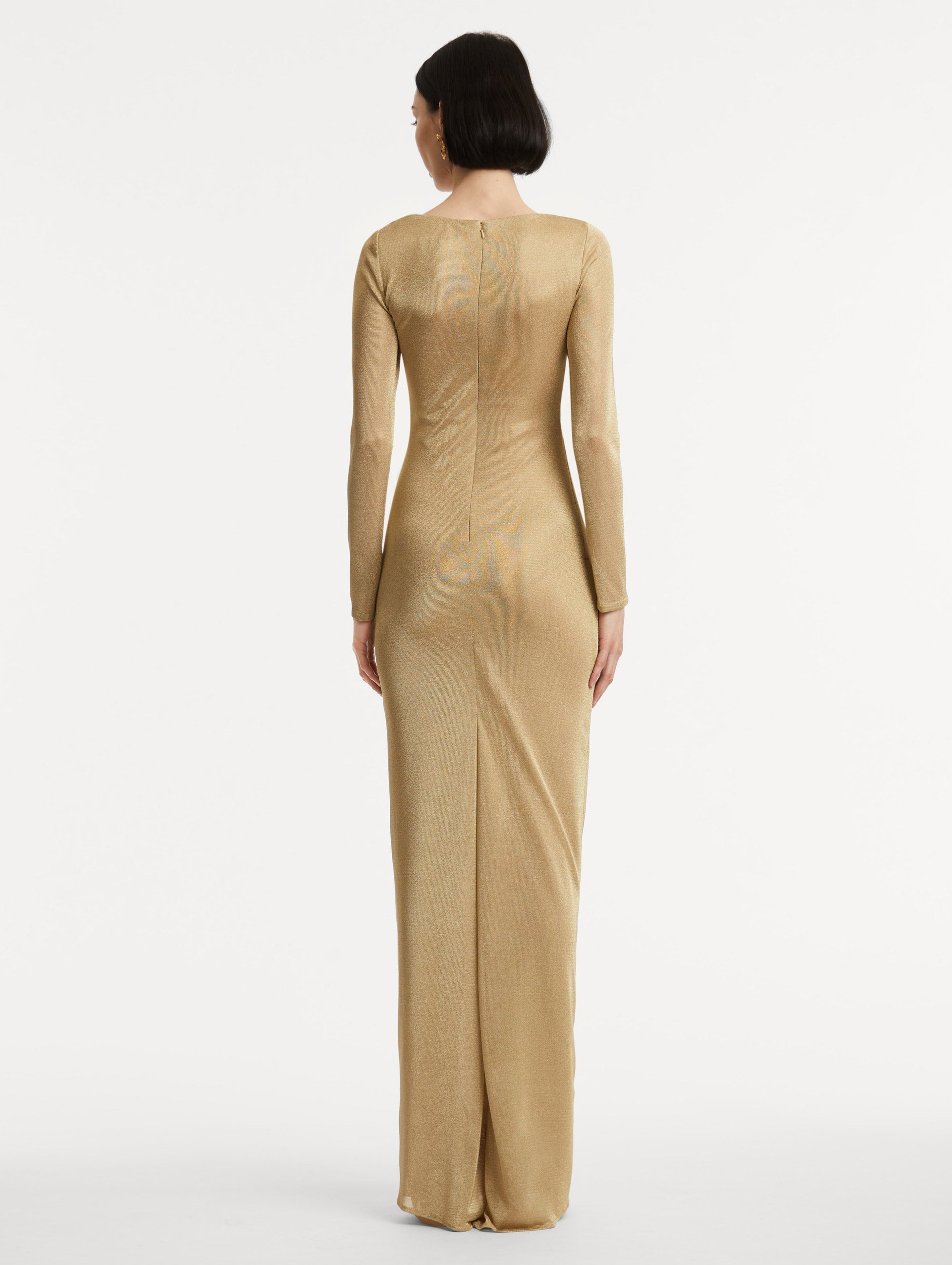 Full body back view image of model wearing a gold metallic jersey gown with a high neckline and long sleeves with draping at the shoulder and waist.