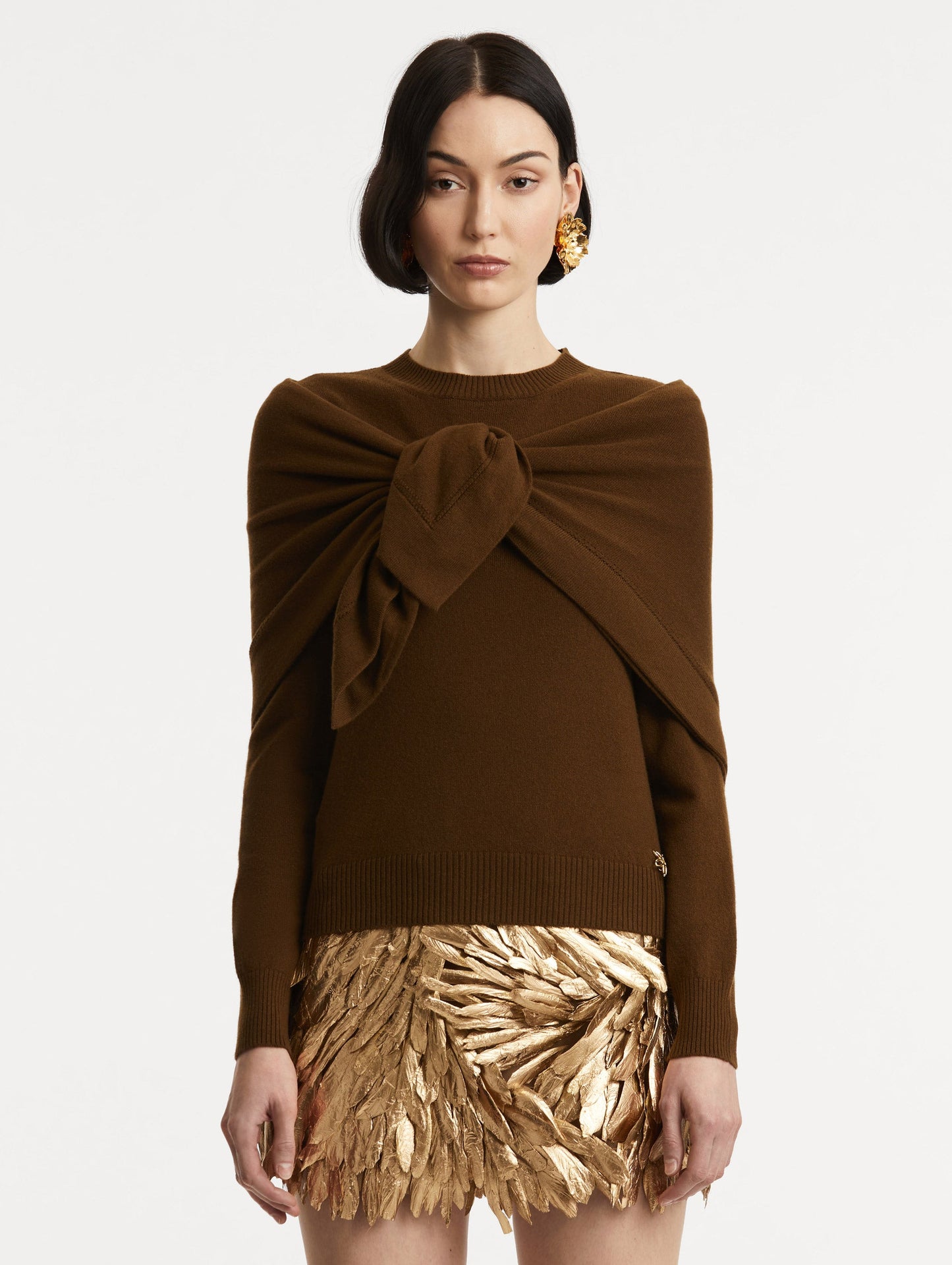 Front view of model wearing brown pullover with long sleeves and a crew neckline. Features 'O' Flower emblem made of the interlocking Oscar 'O' and shawl draped over shoulders and tied in front.