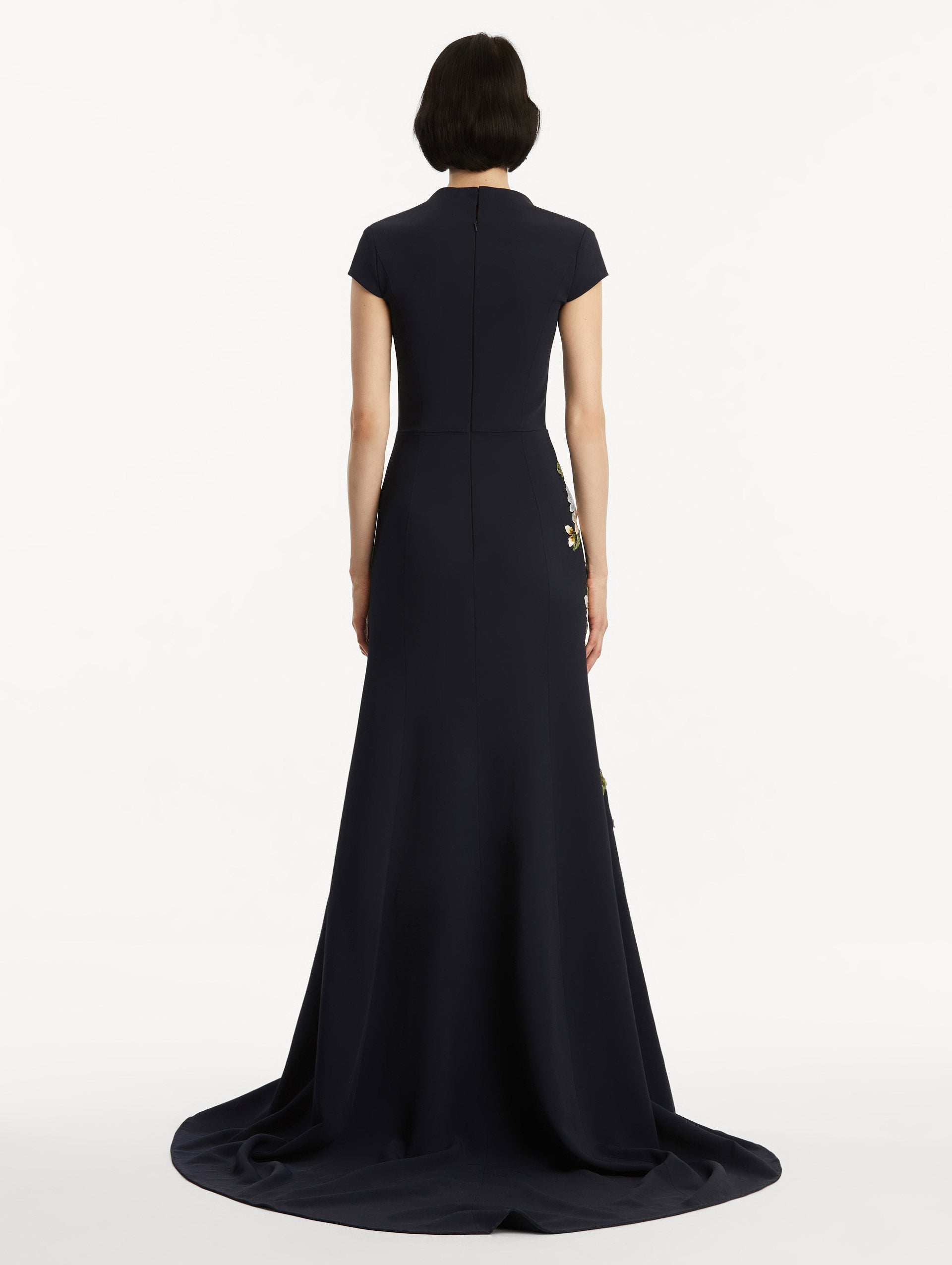 Model wearing short sleeve navy gown with white cherry blossoms embroidered. Back view