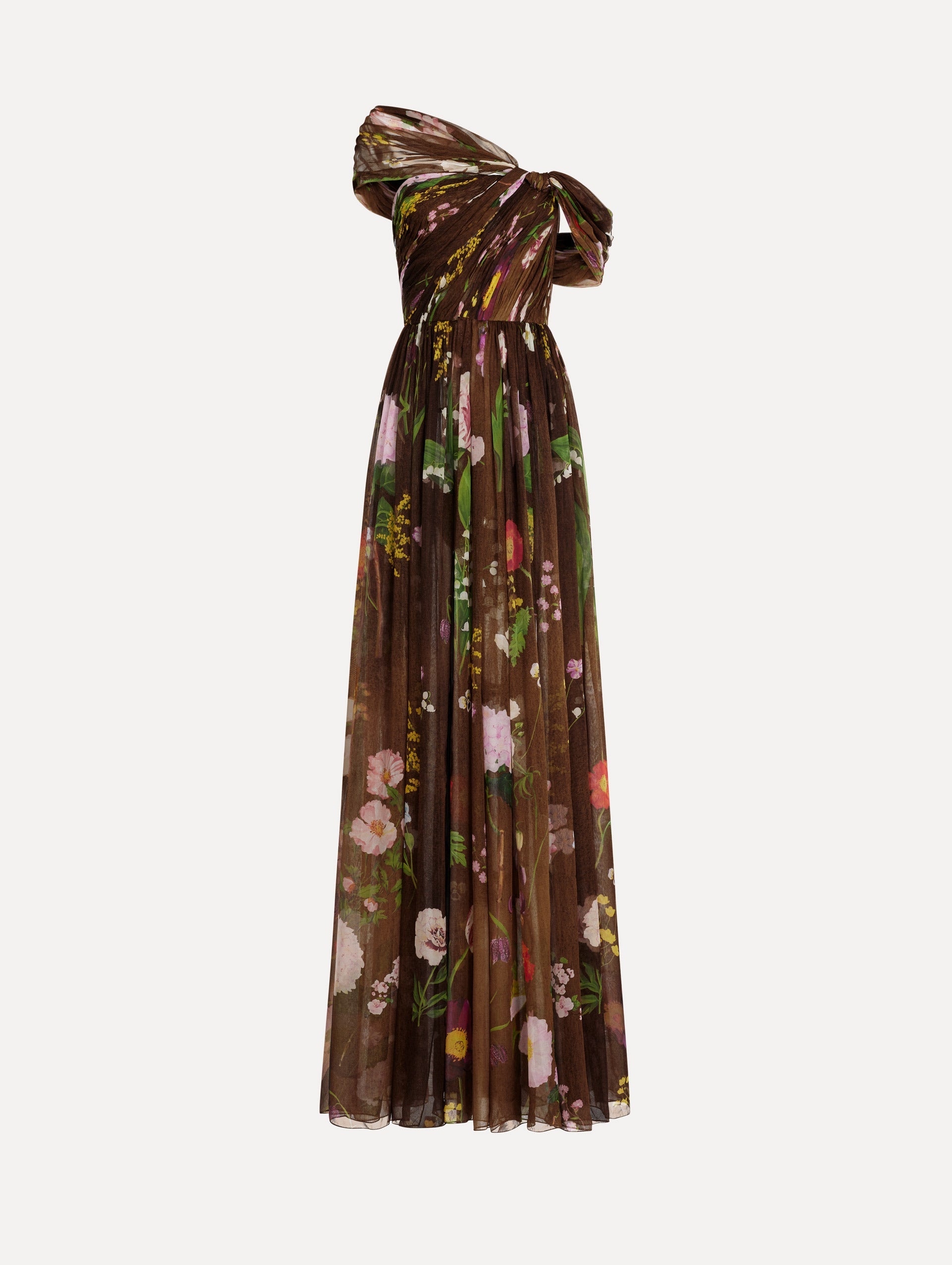 The model is wearing the mixed botanical silk chiffon gown with a one-shoulder neckline and a painterly floral print in a brown multi palette.